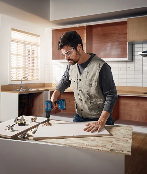 Professional Combo Kit Set: GSR 185-Li + GBH 185-Li + 1 x 18V -2.0Ah + 1 x 18V-4.0Ah + GAL 18V-40 A person wearing safety equipment drills into a wooden board on a kitchen counter.