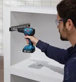 Person wearing safety equipment uses a cordless drill to install drawer slides in a cabinet.