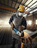 A person wearing safety equipment grinds metal, producing bright sparks in a factory.