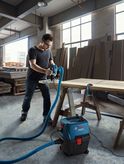 Person using a vacuum extractor with a power tool on wood in a workshop.