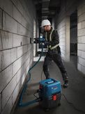 A person wearing safety equipment drills a wall, using a wet/dry extractor for dust.