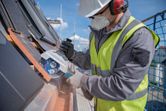 A person wearing safety equipment uses a cordless angle grinder to cut roof tiles.