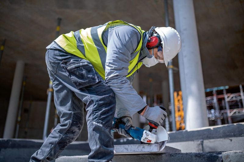 GWS 18V-180 P A person wearing safety equipment grinds concrete with a cordless angle grinder.