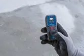 Person wearing safety equipment holds a laser measure on a concrete floor.