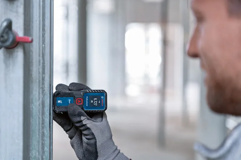 Person wearing safety equipment uses a laser measure to check distance on a metal beam.