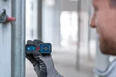 Person wearing safety equipment uses a laser measure to check distance on a metal beam.
