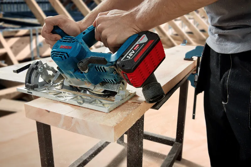 GKS 185-LI Person using a cordless circular saw to cut a wooden board on a workbench.