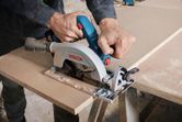 A person cuts wood with a cordless circular saw on a workbench.
