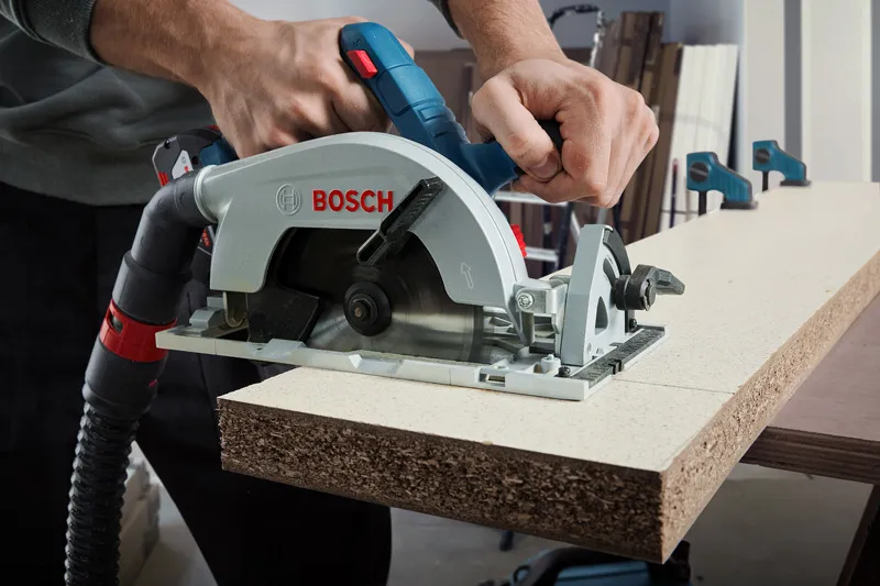 GKS 185-LI A person uses a cordless circular saw to cut particle board.