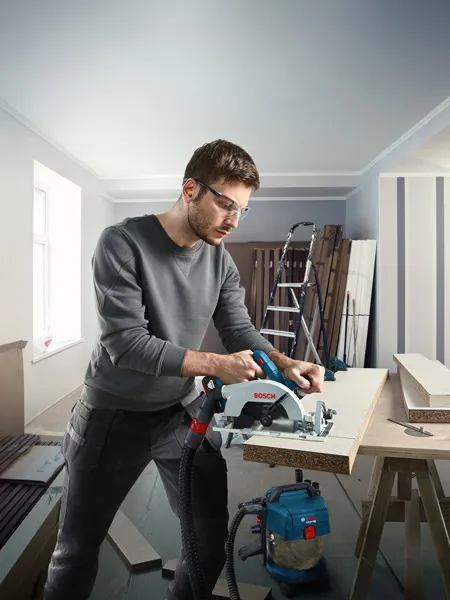GKS 185-LI Person wearing safety equipment cuts wood with a cordless circular saw in a workshop.
