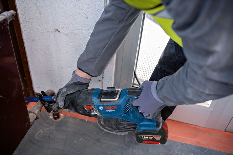 GSA 185-LI A person wearing safety equipment uses a reciprocating saw to cut metal near a door frame.