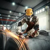 A person wearing safety equipment grinds metal, creating sparks in an industrial setting.