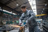 A person wearing safety equipment grinds metal, creating sparks in an industrial workshop.