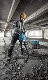 A person wearing safety equipment uses a breaker to demolish concrete flooring.