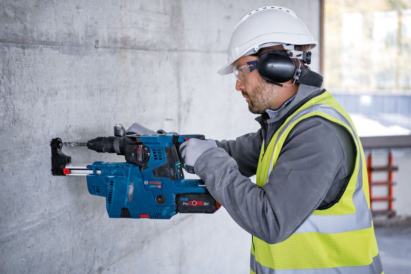 GBH 18V-28 CF A person wearing safety equipment drills into a concrete wall with a cordless rotary hammer.