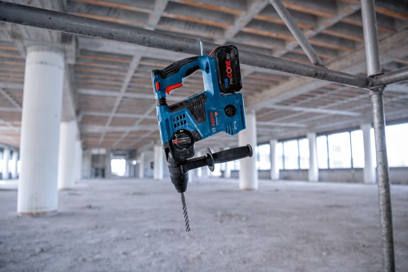 GBH 18V-28 CF Cordless rotary hammer hanging on a metal pipe at an unfinished construction site.