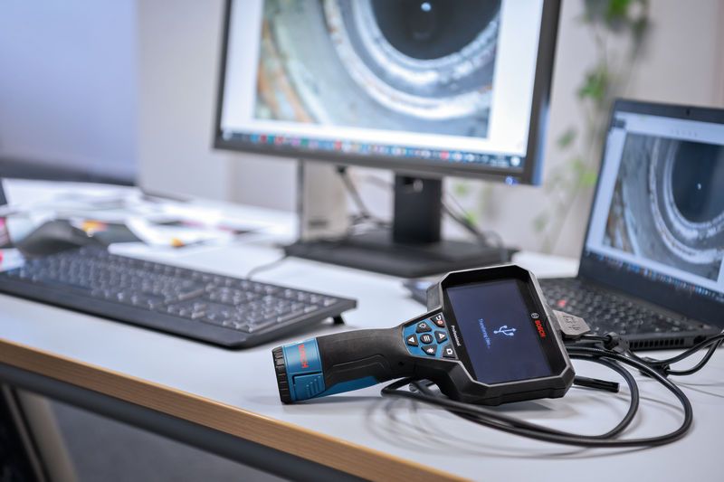 Inspection camera connected to a laptop on an office desk, screen showing pipe interior.