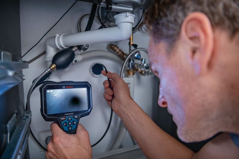 A person inspects plumbing under a sink using an inspection camera.