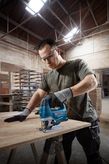Person wearing safety equipment uses a jigsaw to cut wood in a workshop.