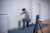 A person marks a wall using a laser leveling tool set on a tripod.