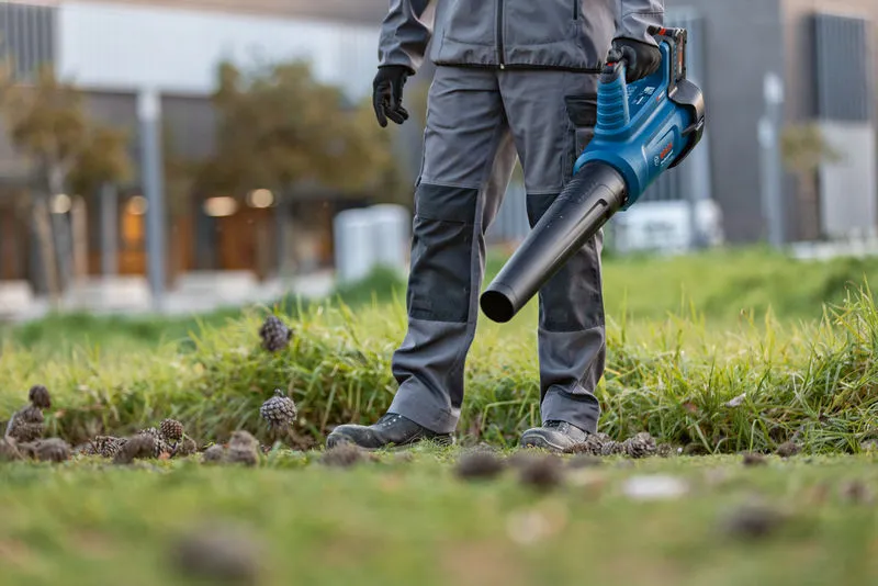 GBL 18V-750 A person wearing safety equipment uses a cordless leaf blower on grassy ground.