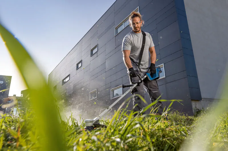 GRT 18V-33 A person wearing safety equipment trims tall grass with a cordless grass trimmer.