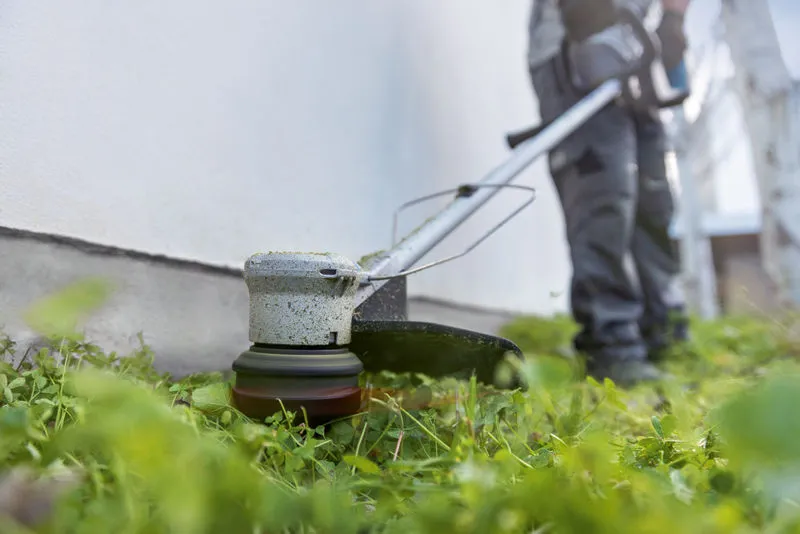GRT 18V-33 A person wearing safety equipment trims grass along a wall using a cordless grass trimmer.
