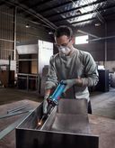 A person wearing safety equipment grinds metal inside an industrial workshop.