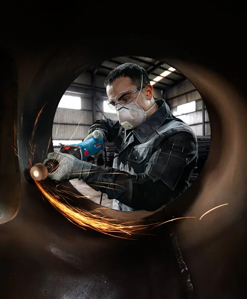 GGS 30 LS A person wearing safety equipment grinds metal inside a large pipe, creating sparks.