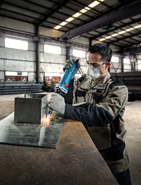 GGS 30 LS A person wearing safety equipment uses a straight grinder on a metal sheet.
