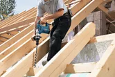 A person drilling into a wooden beam on a roof structure, not wearing safety equipment.