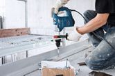 A person wearing safety equipment drills into a metal beam using a rotary hammer.