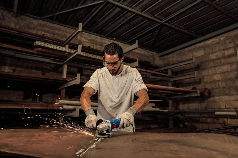 A person wearing safety equipment grinds a metal sheet with an angle grinder.