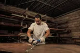 A person wearing safety equipment grinds a metal sheet with an angle grinder.