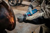 A person wearing safety equipment grinds metal, creating bright sparks.