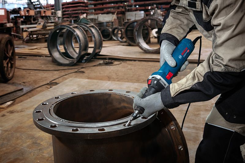 GGS 30 LS A person wearing safety equipment grinds the edge of a large metal pipe with a straight grinder.