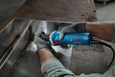 A person wearing safety equipment grinds a welded metal seam with a straight grinder.