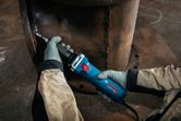 A person wearing safety equipment grinds a weld seam on a large metal pipe.