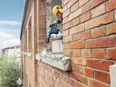 A person wearing safety equipment drills into a brick window frame.