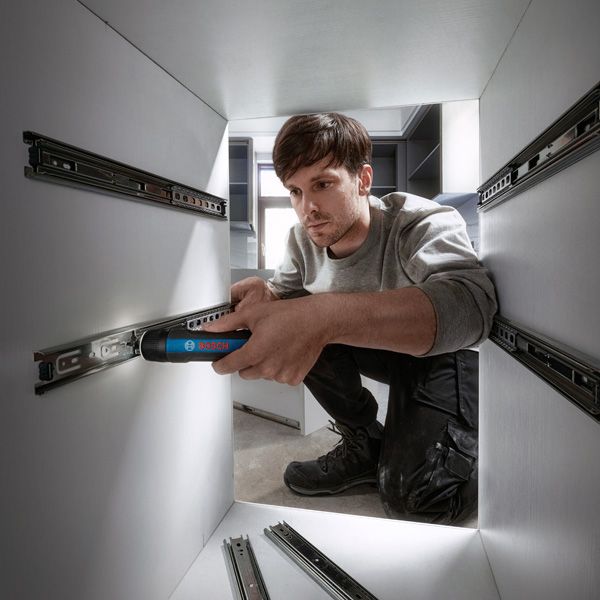 A person installs drawer slides in a cabinet using a cordless screwdriver.