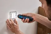 A person uses a cordless screwdriver to fasten screws on a light switch panel.