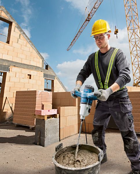GRW 140 A person wearing safety equipment mixes cement with a stirring mechanism at a construction site.