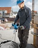 A person wearing safety equipment mixes material with an electric stirring mechanism.
