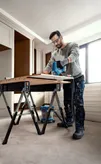 A person wearing safety equipment uses a jigsaw to cut wood on a workbench.