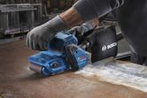 A person wearing safety equipment uses a belt sander on a metal surface.