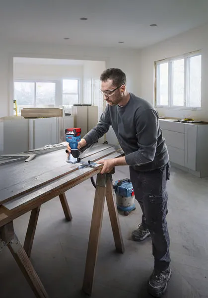 A person wearing safety equipment uses a router to shape wood on a work table.