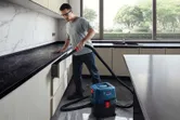 A person wearing safety equipment cleans kitchen drawers with a wet dry extractor.