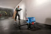 A person wearing safety equipment drills into a wall, wet-dry extractor connected nearby.