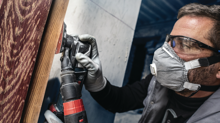 PRO F460 Sanding Sheet, 93 x 93 mm, G60, G80, G120, G180, G240, 10 pcs Person wearing safety equipment sands a wooden surface with a power tool.