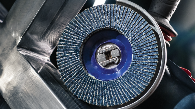 PRO X571 Flap Disc, Straight, 125 mm, G40, X-Lock A blue flap disc grinds metal, with tool held near a steel surface.